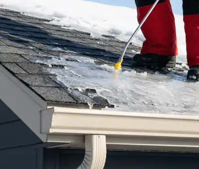Ice dam removal technician using a steam wand to melt thick ice buildup on a residential roof in Boulder, CO