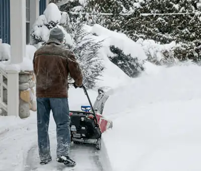 Residential snow removal technician using a snow blower to clear a home driveway and walkway in Boulder, CO