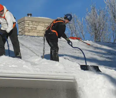 Professional technicians performing roof snow removal with safety harnesses and shovels in Boulder, CO